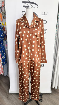 A two-piece pajama set displayed on a mannequin torso in a retail setting. The pajama set consists of a long-sleeve button-up top and matching pants in a brown satin-like fabric with a cream polka dot pattern.