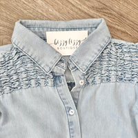 Light blue denim shirt with ruffled collar on a wooden surface, featuring 'bizzy lizzy boutique' label.