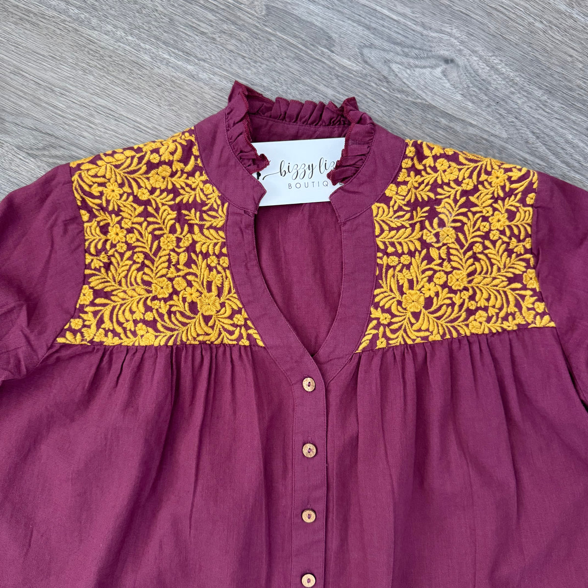 Maroon blouse with yellow floral embroidered patterns on a gray surface
