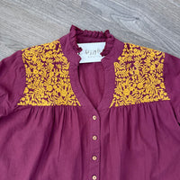 Maroon blouse with yellow floral embroidered patterns on a gray surface