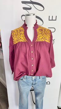 Mannequin wearing a maroon blouse with yellow embroidery details and blue jeans against a white background.