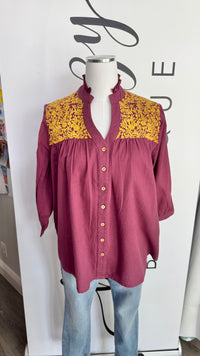 Mannequin wearing a maroon blouse with yellow embroidered details against a white background