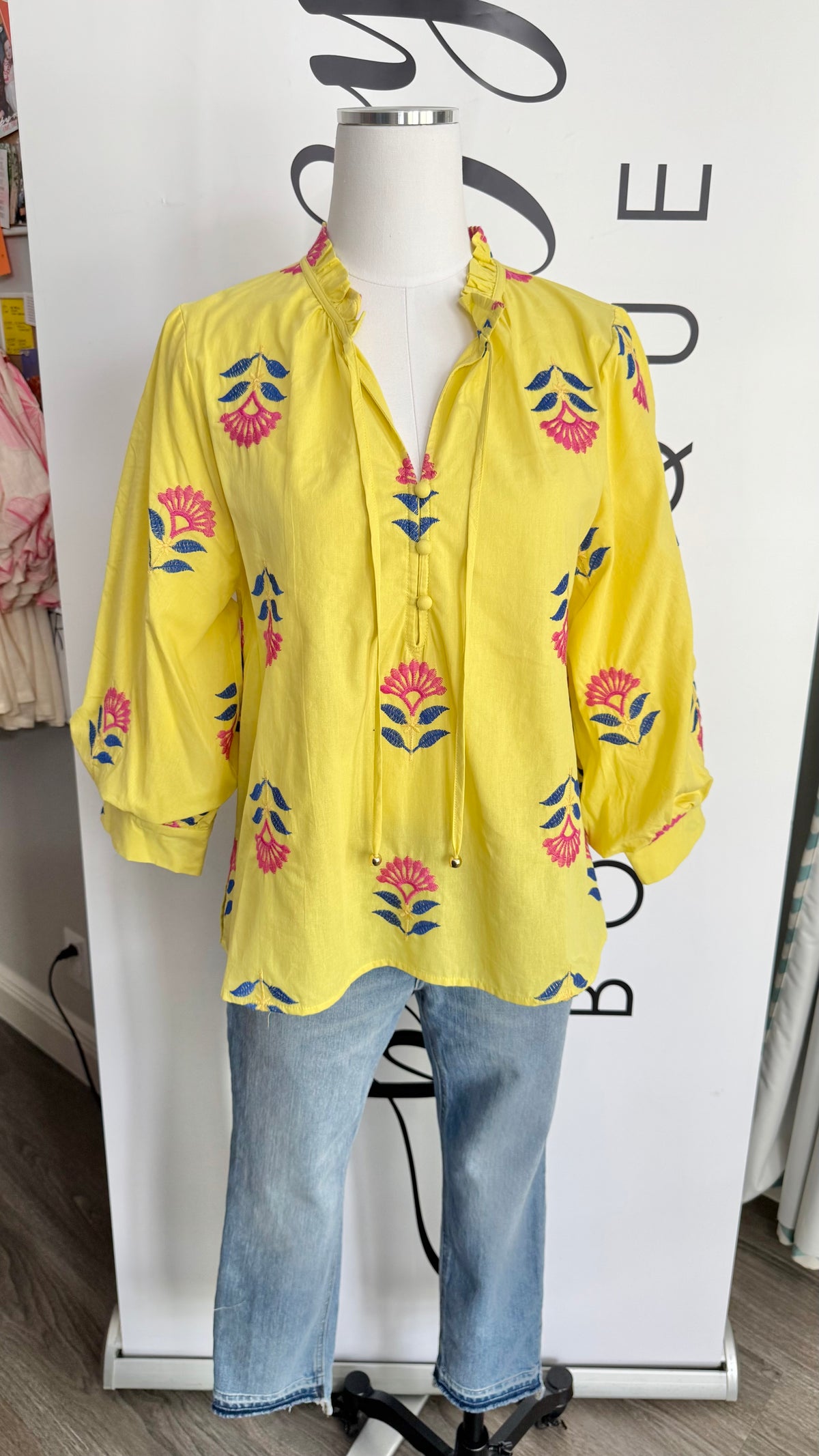 Yellow floral blouse on a mannequin with blue jeans against a white background
