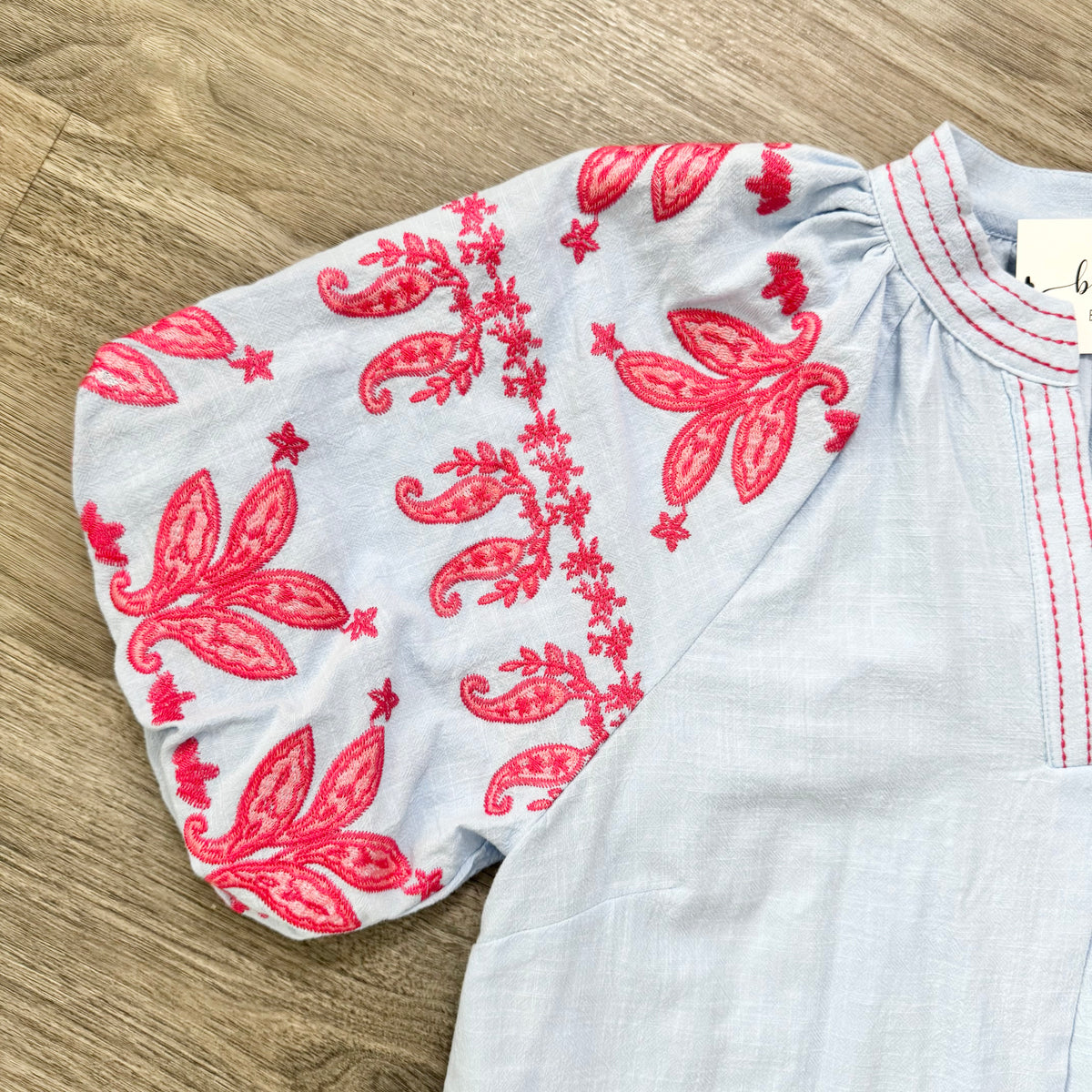 Light Blue Top with red floral embroidery on a wooden surface