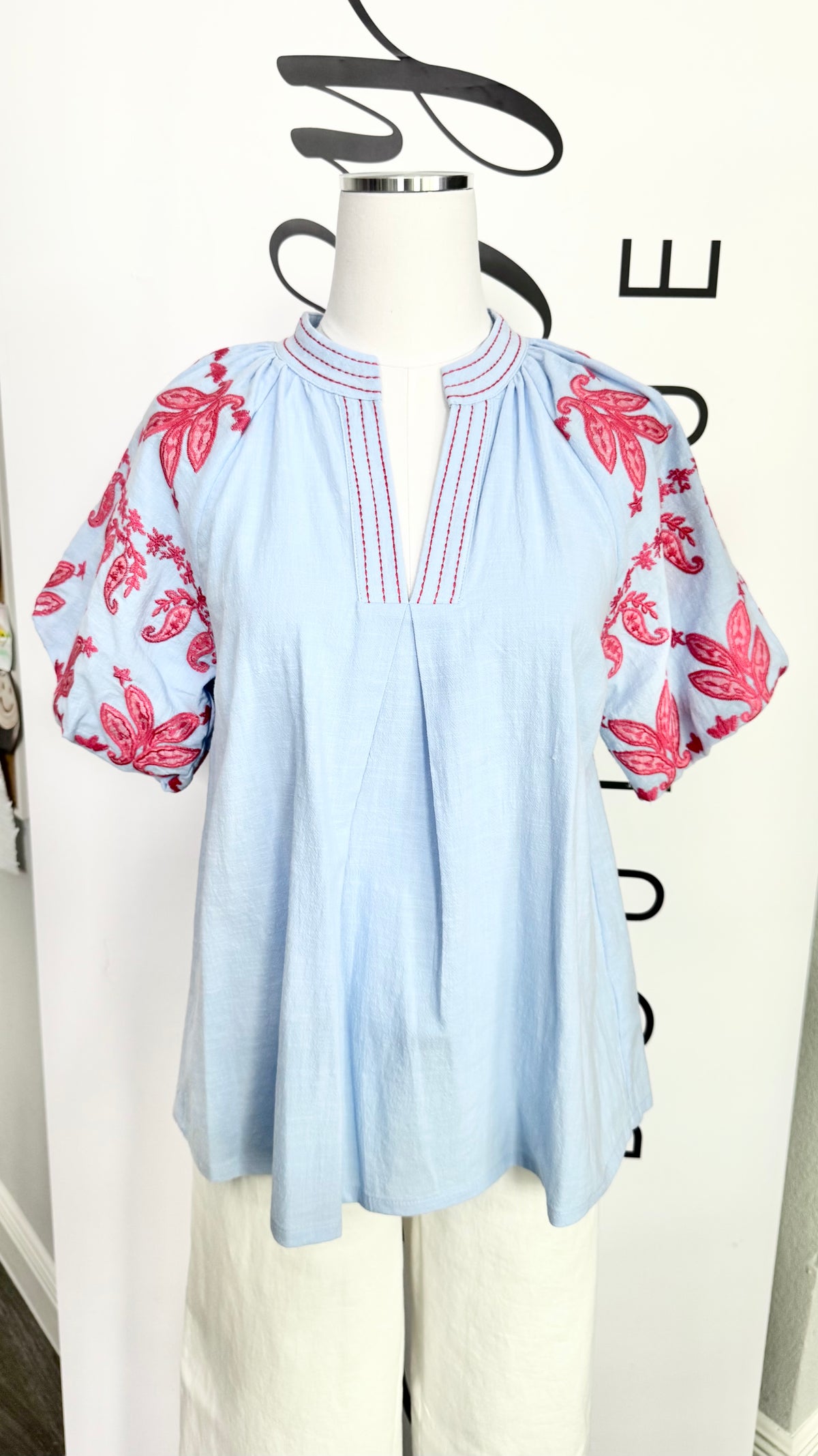 Light blue blouse with pink floral sleeves on a mannequin against a white background
