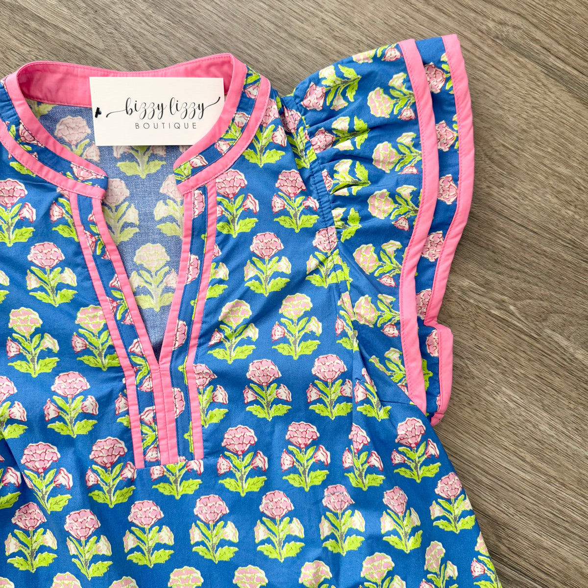 Floral-patterned dress with pink trim on a wooden surface, featuring a 'Bizzy Lizzy Boutique' tag.