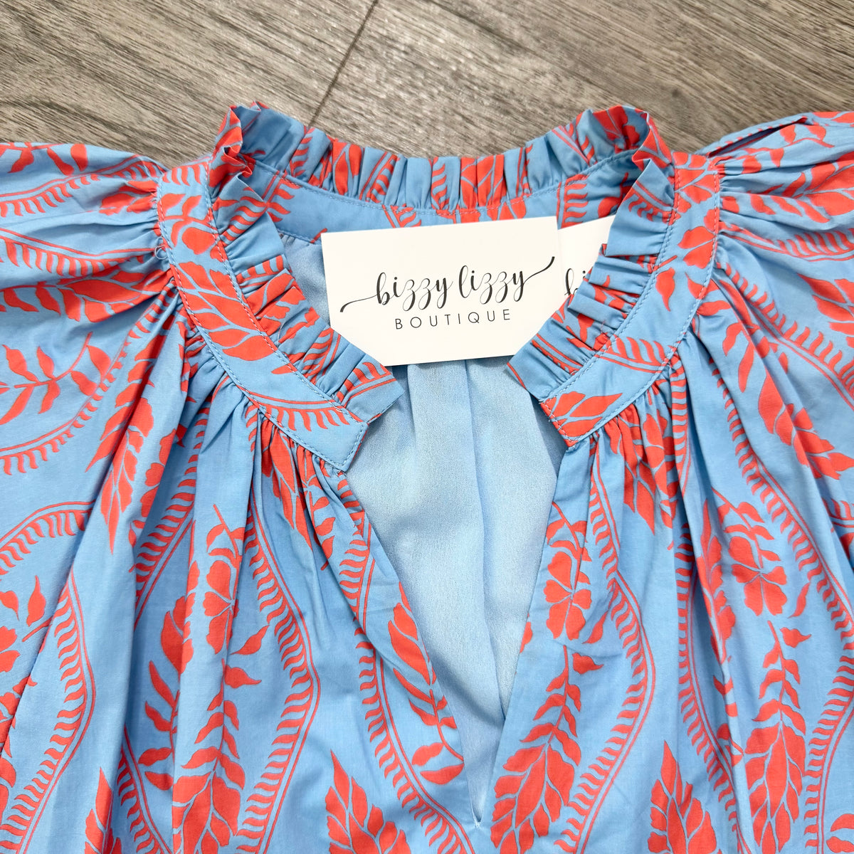 Blue and orange patterned top with a tag from Lizzy Lizzy Boutique on a wooden surface.