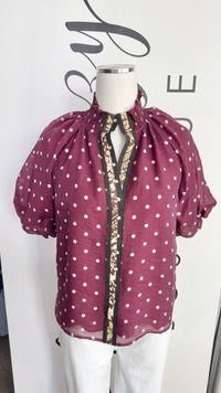 A sheer burgundy short-sleeve blouse with white polka dots and a floral-print center placket, displayed on a white mannequin torso.