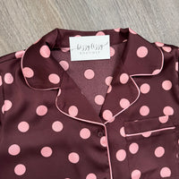 A close-up of a women's pajama top in dark burgundy with light pink polka dots and matching pink piping, featuring a white neck label that reads 'bizzy lizzy boutique'.