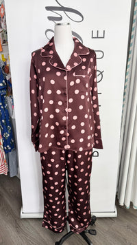 A two-piece long-sleeve pajama set displayed on a mannequin torso, featuring a maroon satin-like fabric with light pink polka dots. The set includes a button-front top with a collar and matching wide-leg pants.
