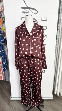 A two-piece satin pajama set with a maroon base and pink polka dots, displayed on a white mannequin torso in a boutique setting.