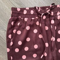 A close-up of maroon drawstring pants with a pink polka dot pattern, laid flat on a gray wood-textured surface.