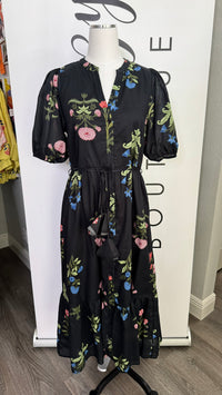 A black midi dress with a colorful floral print, displayed on a mannequin in front of a white boutique sign.