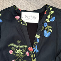 Close-up of a black floral blouse with embroidered pink, blue, and green botanical details, featuring a white neck label that reads 'bizzy lizzy BOUTIQUE'.