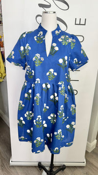 A blue short-sleeve dress with a white and green floral print, displayed on a mannequin in front of a white boutique backdrop.
