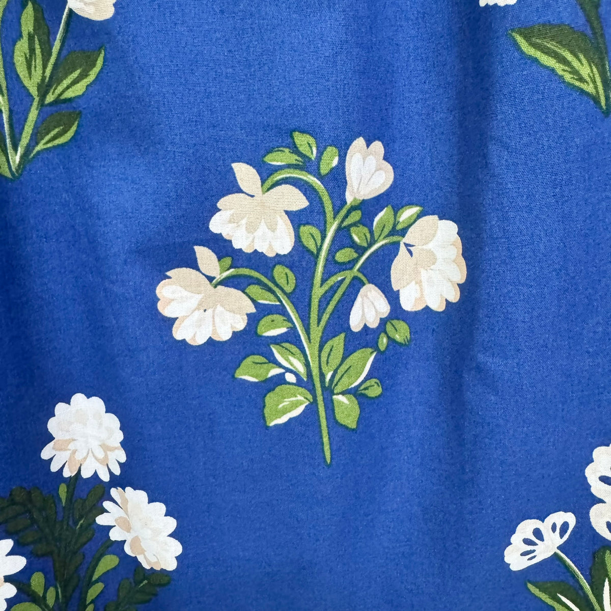 A close-up of a blue fabric with a repeating floral pattern featuring white flowers and green leaves.