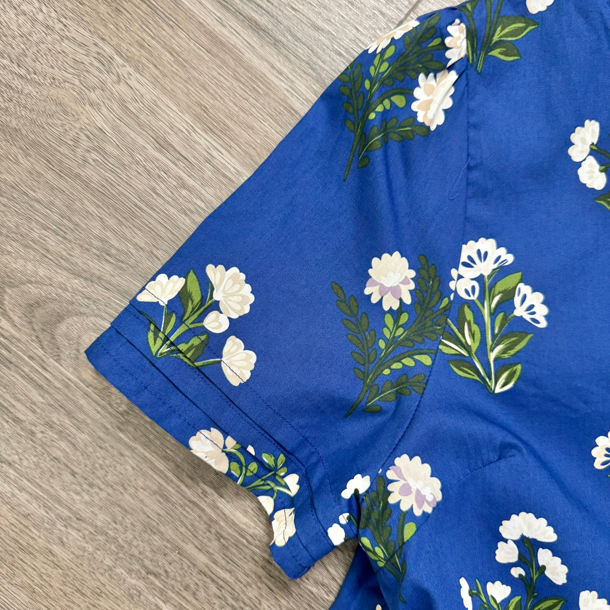 A close-up of a royal blue dress  laid flat on a light wood floor, featuring a white and green floral print.