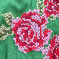 Close-up of a green knitted fabric featuring a large pink and red floral pattern with light green leaves.