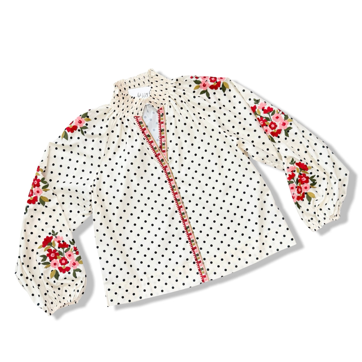 A women's long-sleeve blouse with a white base, black polka dots, and red floral prints on the shoulders and sleeves, featuring a red patterned trim along the front placket.