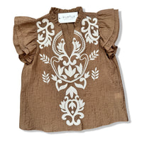 A brown textured cotton blouse with white embroidered floral patterns on the front, featuring ruffled short sleeves and a V-neckline, laid flat on a white background.
