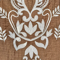 Close-up of a brown textured fabric with white embroidered floral and scroll motifs.