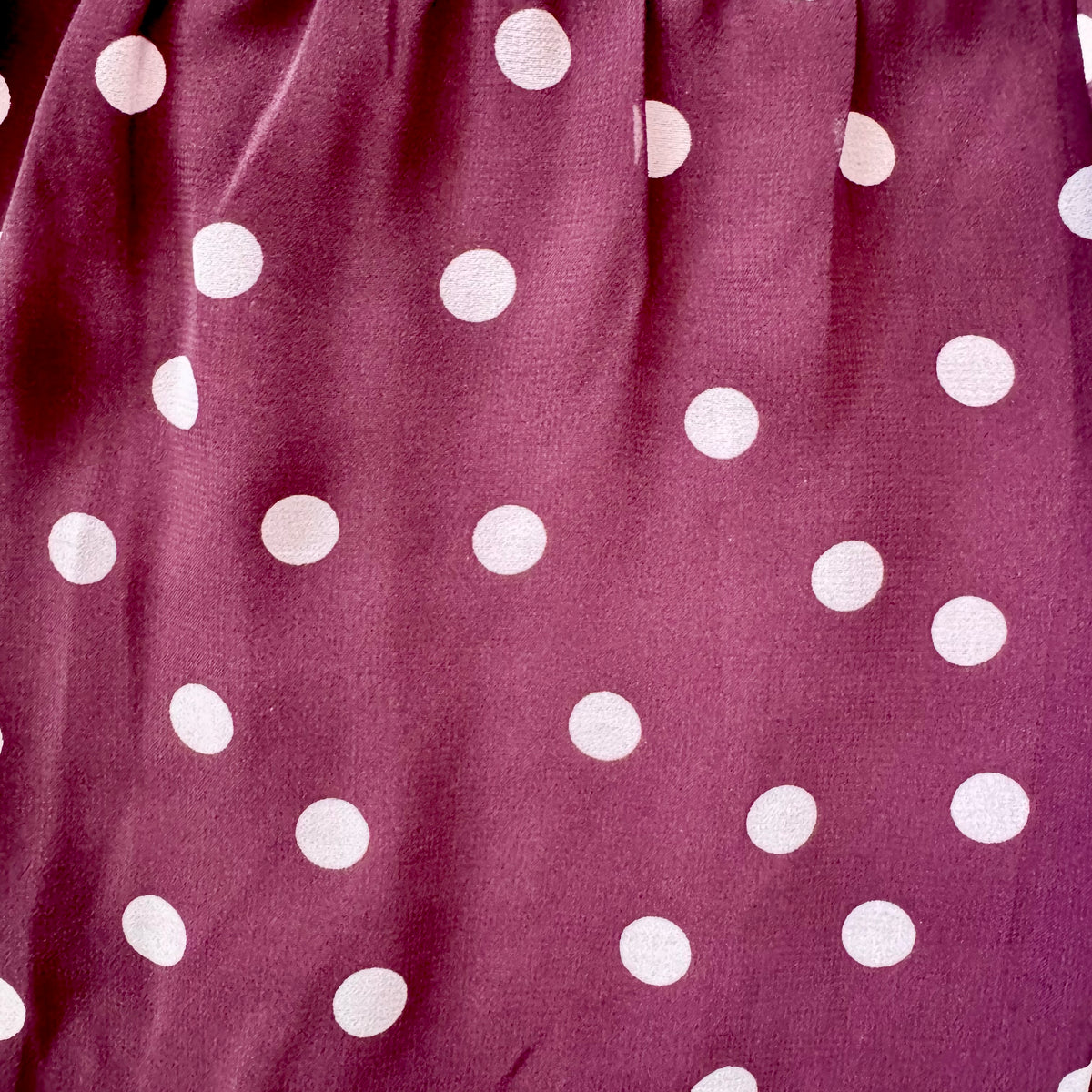 A close-up of a fabric surface in a muted mauve-purple color with evenly spaced white polka dots.