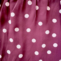A close-up of a fabric surface in a muted mauve-purple color with evenly spaced white polka dots.