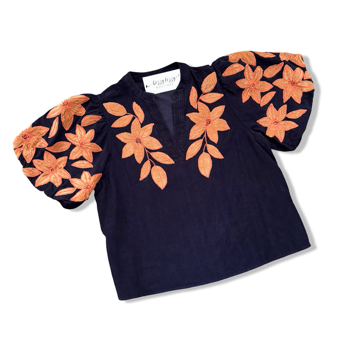 A navy blue short-sleeve blouse with voluminous puff sleeves and large orange floral embroidery and applique on the shoulders and chest, displayed on a white background.