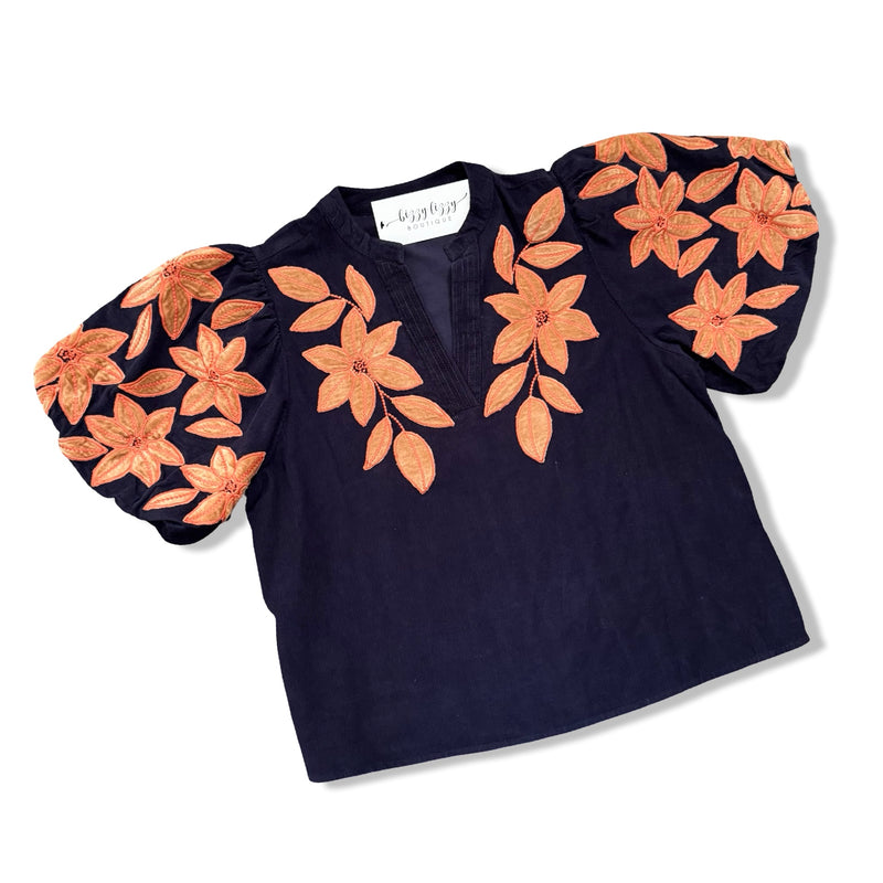 A navy blue short-sleeve blouse with voluminous puff sleeves and large orange floral embroidery and applique on the shoulders and chest, displayed on a white background.