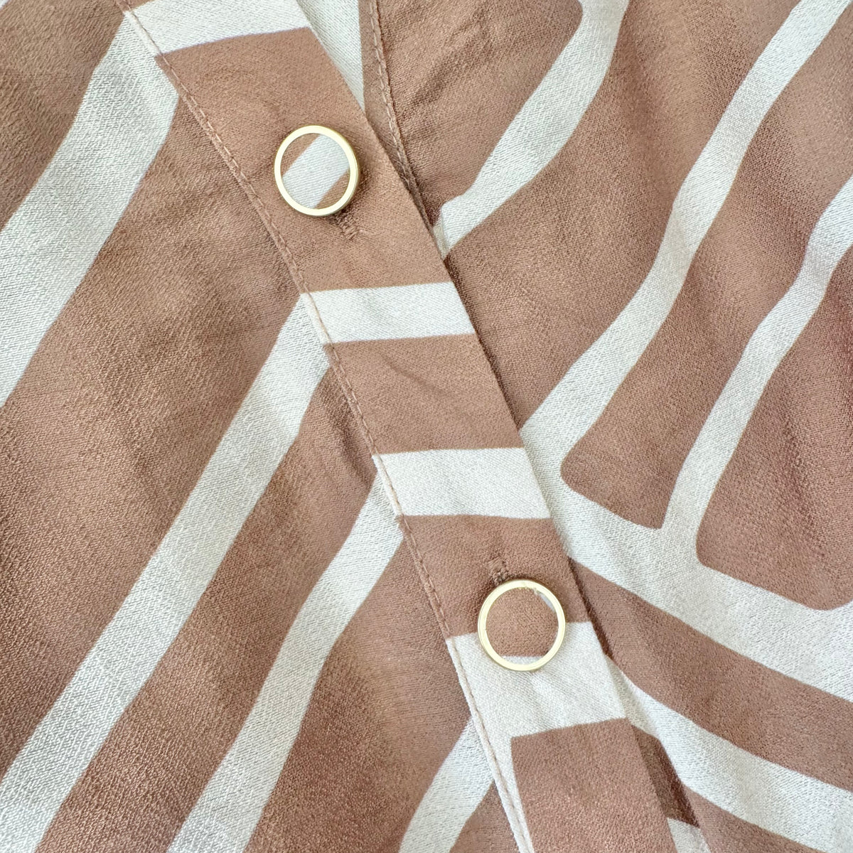 Close-up of a brown and white striped fabric garment with gold-tone metal grommets on the front closure.