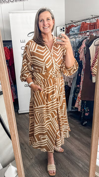 A woman takes a mirror selfie in a clothing boutique wearing a brown and beige geometric patterned midi dress with three-quarter sleeves and a V-neckline.
