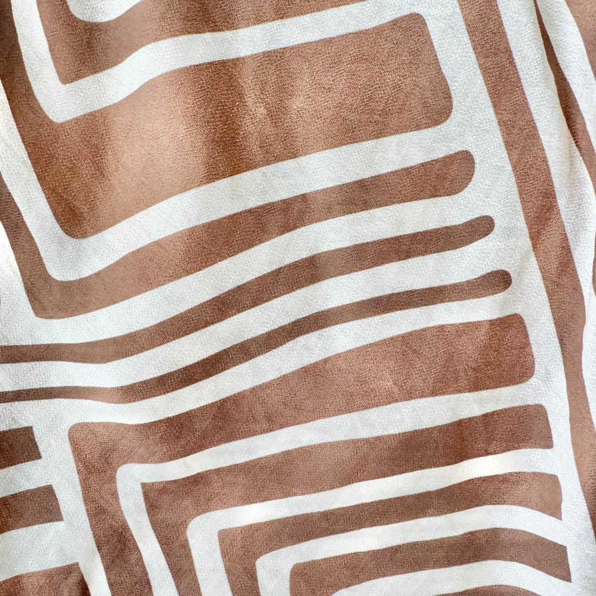 A close-up of a textile with a geometric pattern of wavy tan and off-white stripes.