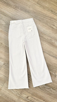 White wide-leg cropped jeans laid flat on a light brown wood floor, showing the back pockets and a small white brand label.