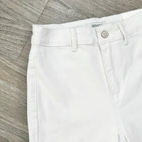 White denim shorts laid flat on a gray wood-look floor, showing the waistband, button closure, belt loops, and part of the Zenith brand label.