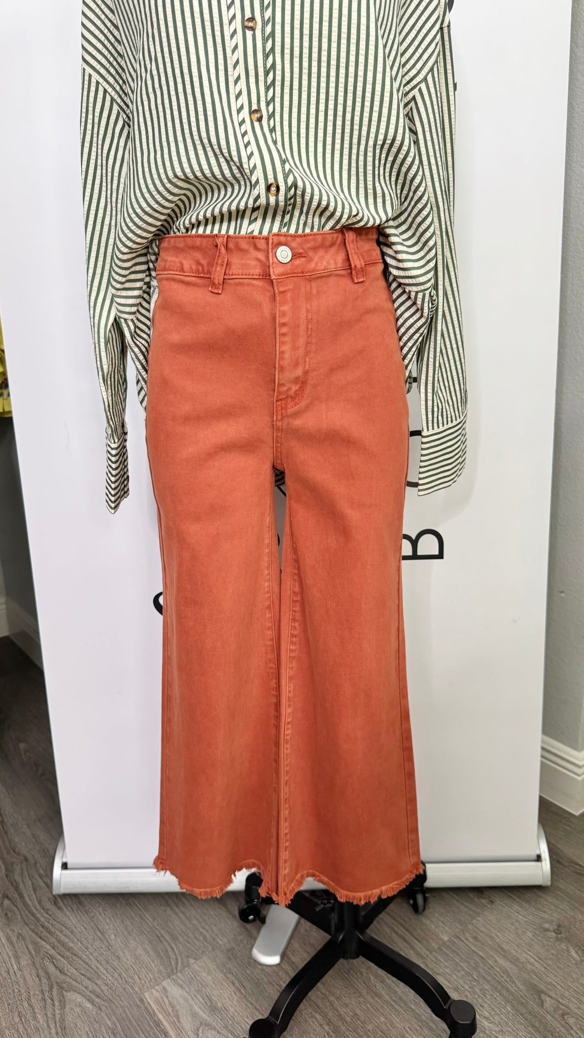 A rust-orange denim midi skirt with a front slit, styled with a green and white striped long-sleeve shirt on a dress form mannequin.