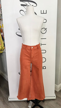 A pair of wide-leg, high-waisted orange denim jeans displayed on a white mannequin torso. The jeans feature a single front button closure and a raw, frayed hem.